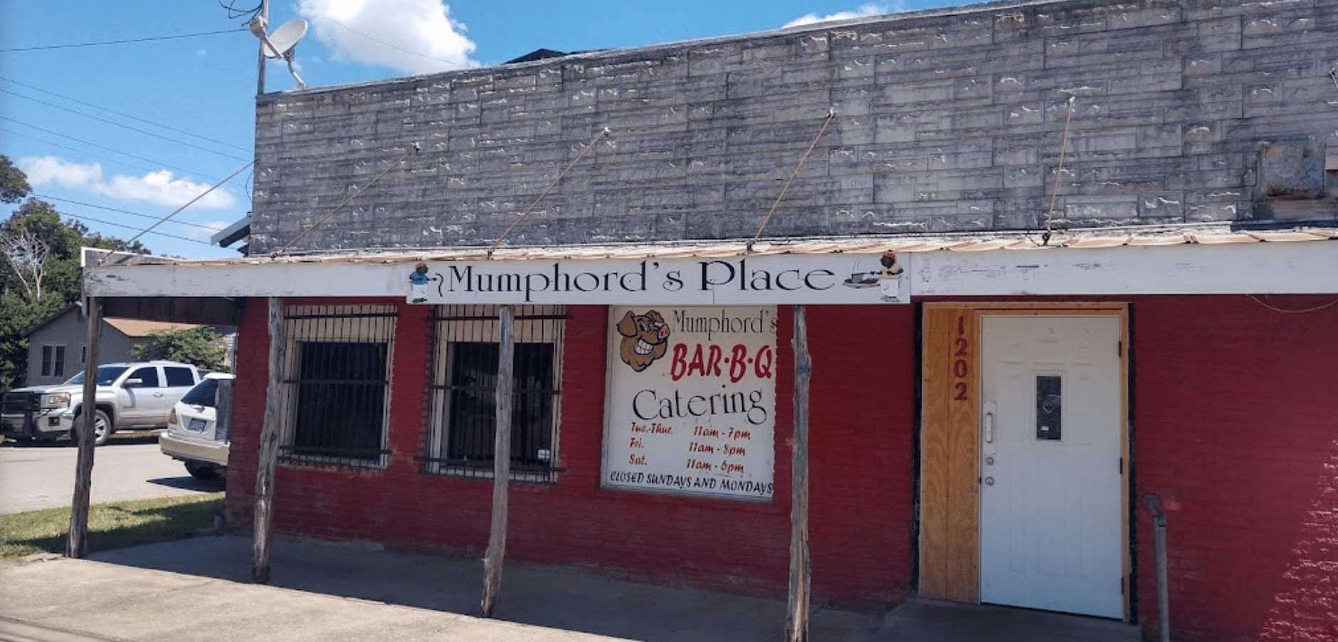 Small red storefront with faded sign, white door, and graffiti under a bright blue sky