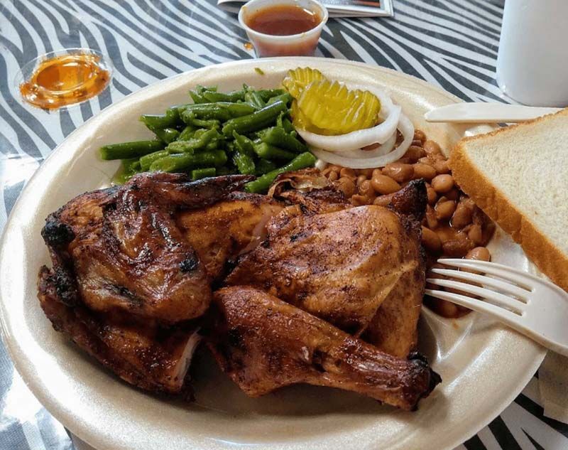 Grilled chicken dinner with green beans, beans, onion, bread, and dipping sauce on a plate