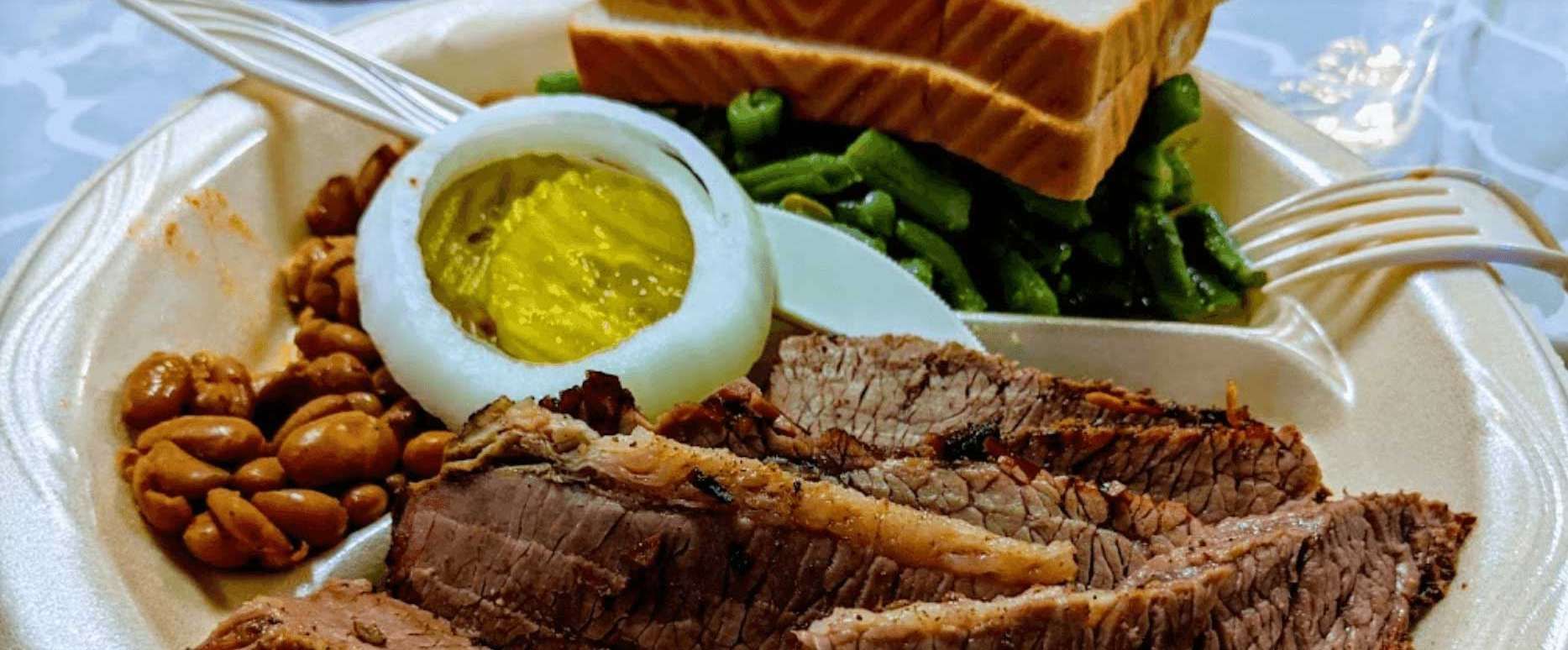 Plated roast beef with boiled egg, potatoes, greens, beans, and bread on a white dish