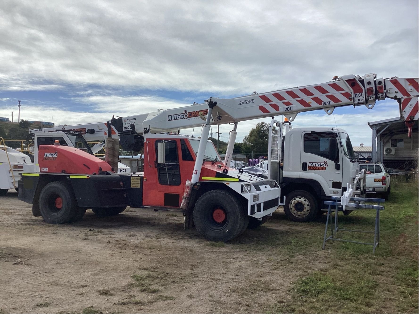 Two utility trucks with extended booms parked on a dirt lot under a cloudy sky - King Cranes in Bowen QLD
