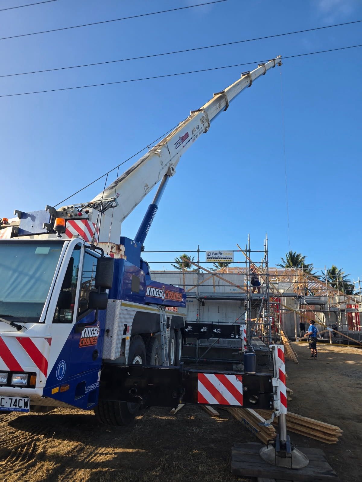 Crane lifting materials at a construction site beside a partially built house under a clear blue sky - King Cranes in Bowen QLD