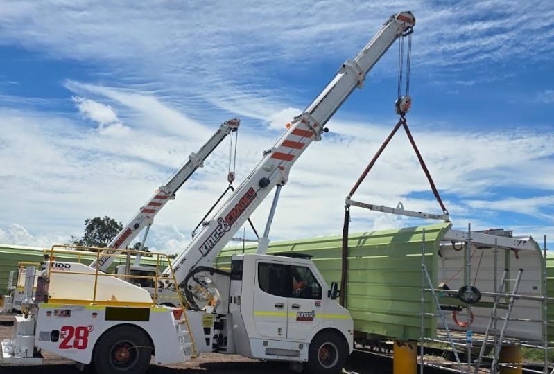 Two Boom Trucks Lifting a Large Green Tank in a Yard — Kings Cranes in Bowen, QLD