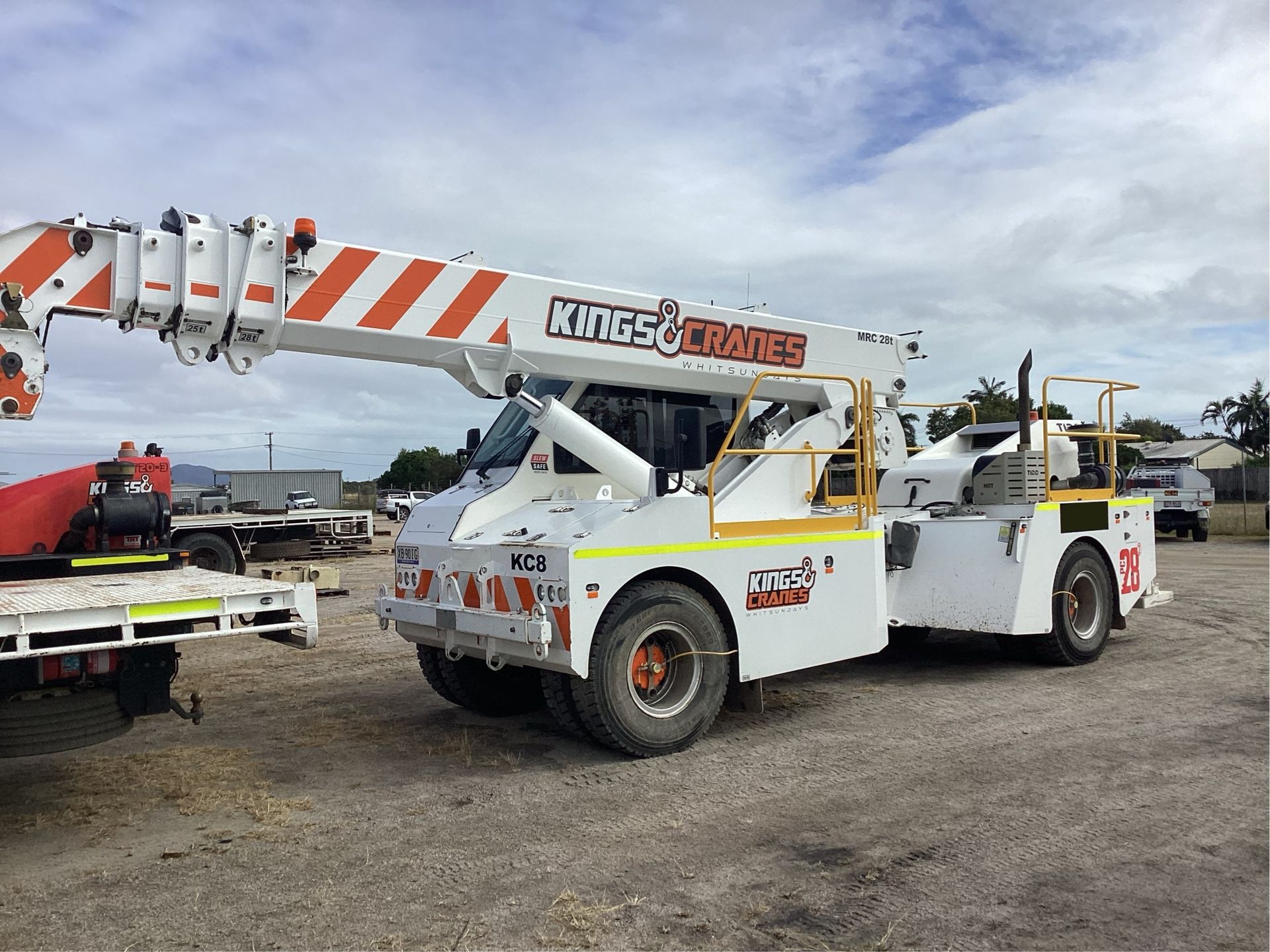 White Crones crane truck parked on gravel under a cloudy sky, with a flatbed truck beside it. - King Cranes in Bowen QLD