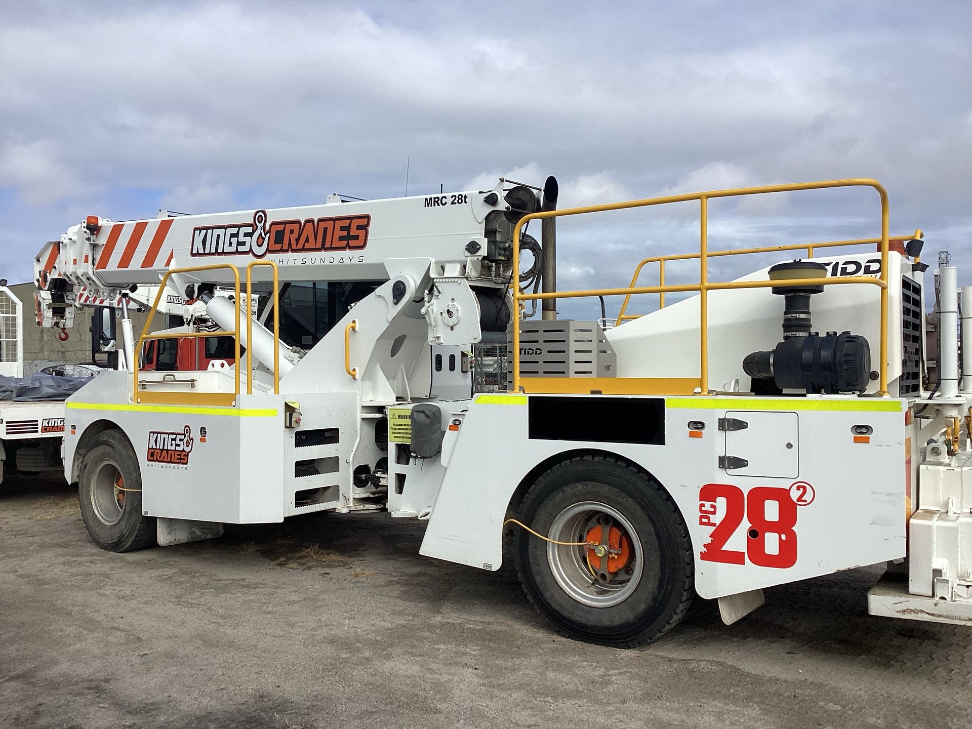 White utility boom truck with yellow rails and red number 28 parked outdoors on gravel. - King Cranes in Bowen QLD