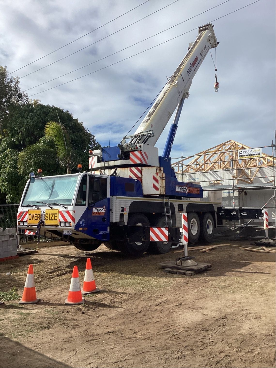 Blue-and-white crane truck at a construction site with orange cones and a building frame in the background - King Cranes in Bowen QLD