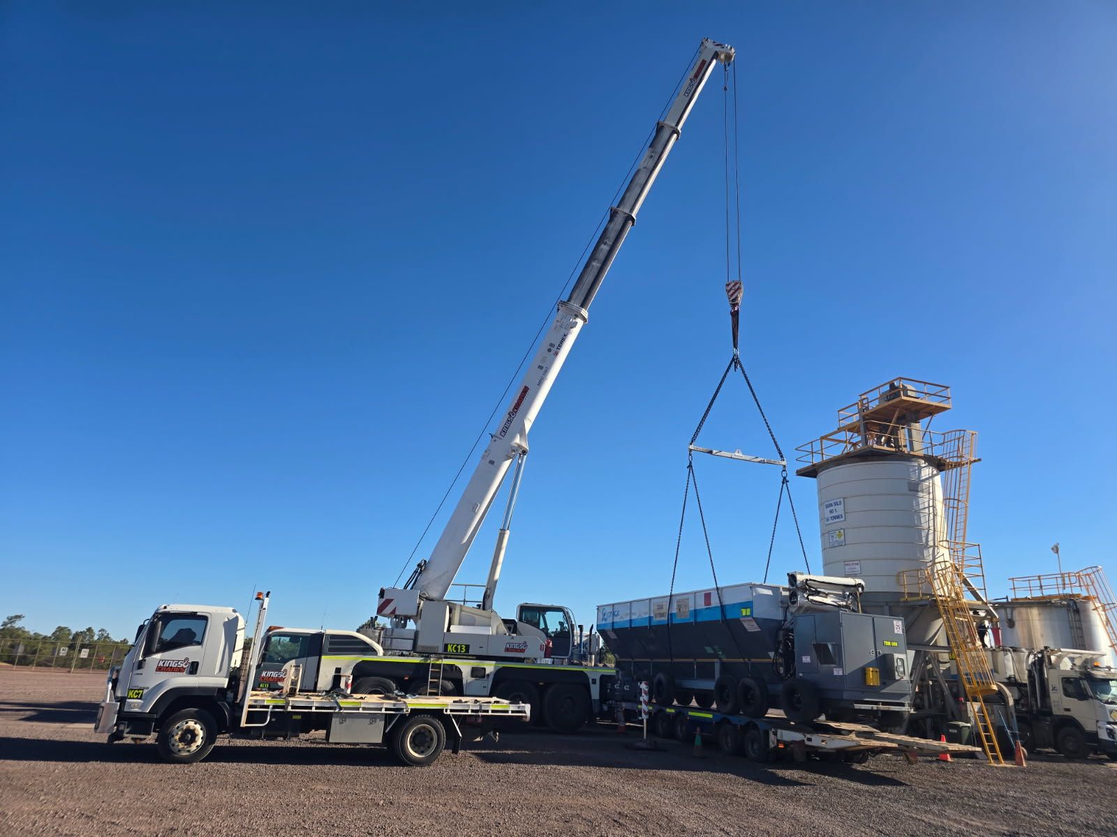 Two white cranes lifting a long green industrial structure outdoors under a blue sky — Kings Cranes in Proserpine, QLD
