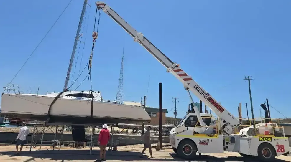 Crane lifting a boat onto a trailer in a sunlit lot with workers nearby under a clear blue sky — Kings Cranes in Airlie Beach, QLD