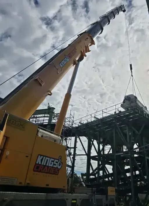 Yellow Kingsey crane lifting at a construction site beside a steel structure under a cloudy sky — Kings Cranes in Collinsville, QLD