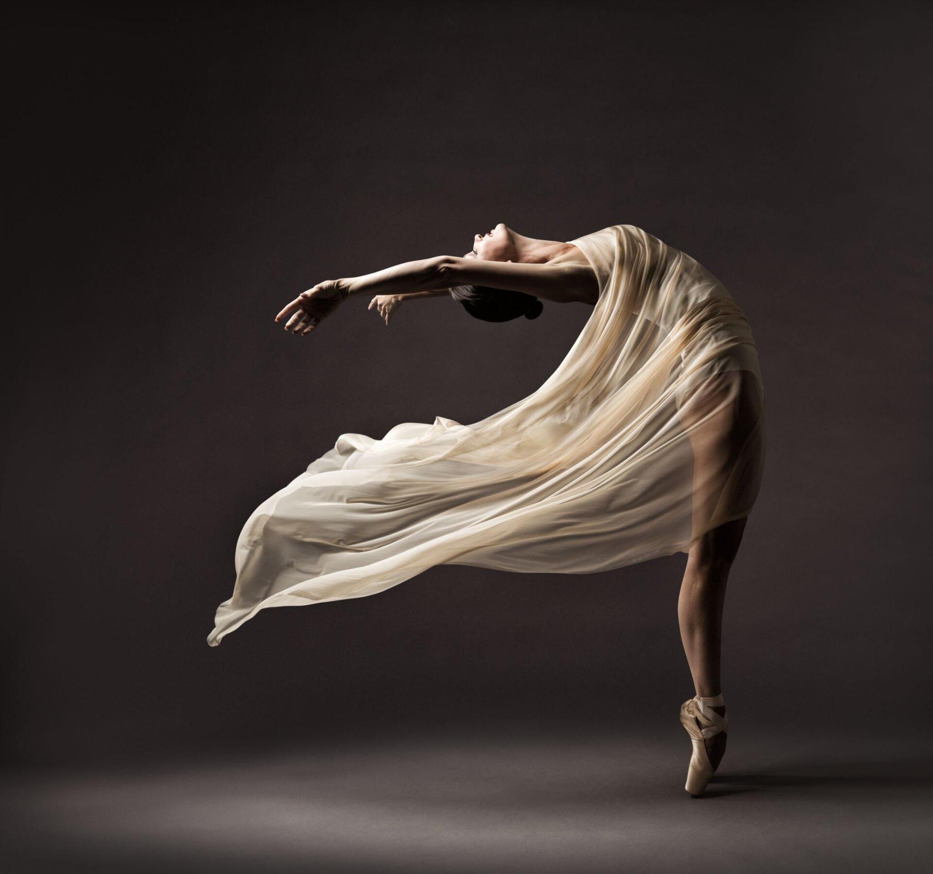 A ballerina in a white dress and pointe shoes is dancing