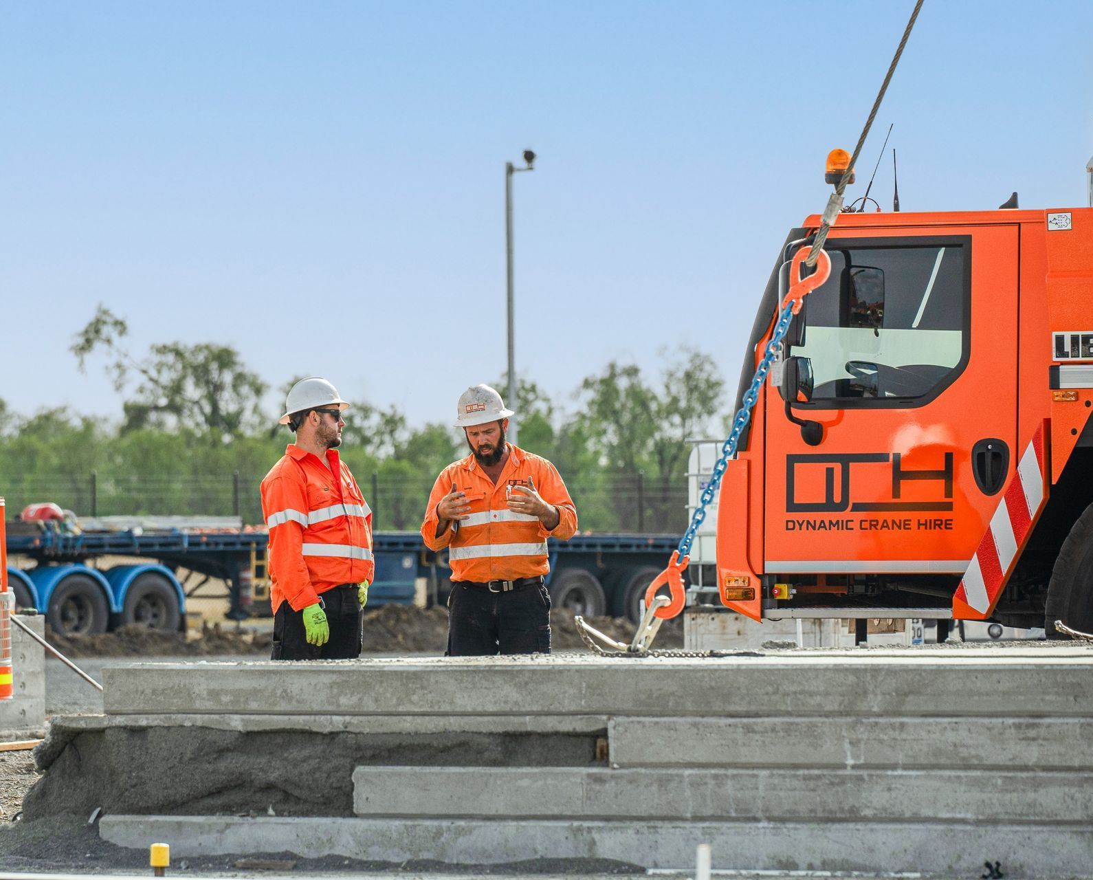 Two Construction Workers Are Standing In Front Of An Orange Truck — Dynamic Crane Hire In Middlemount, QLD