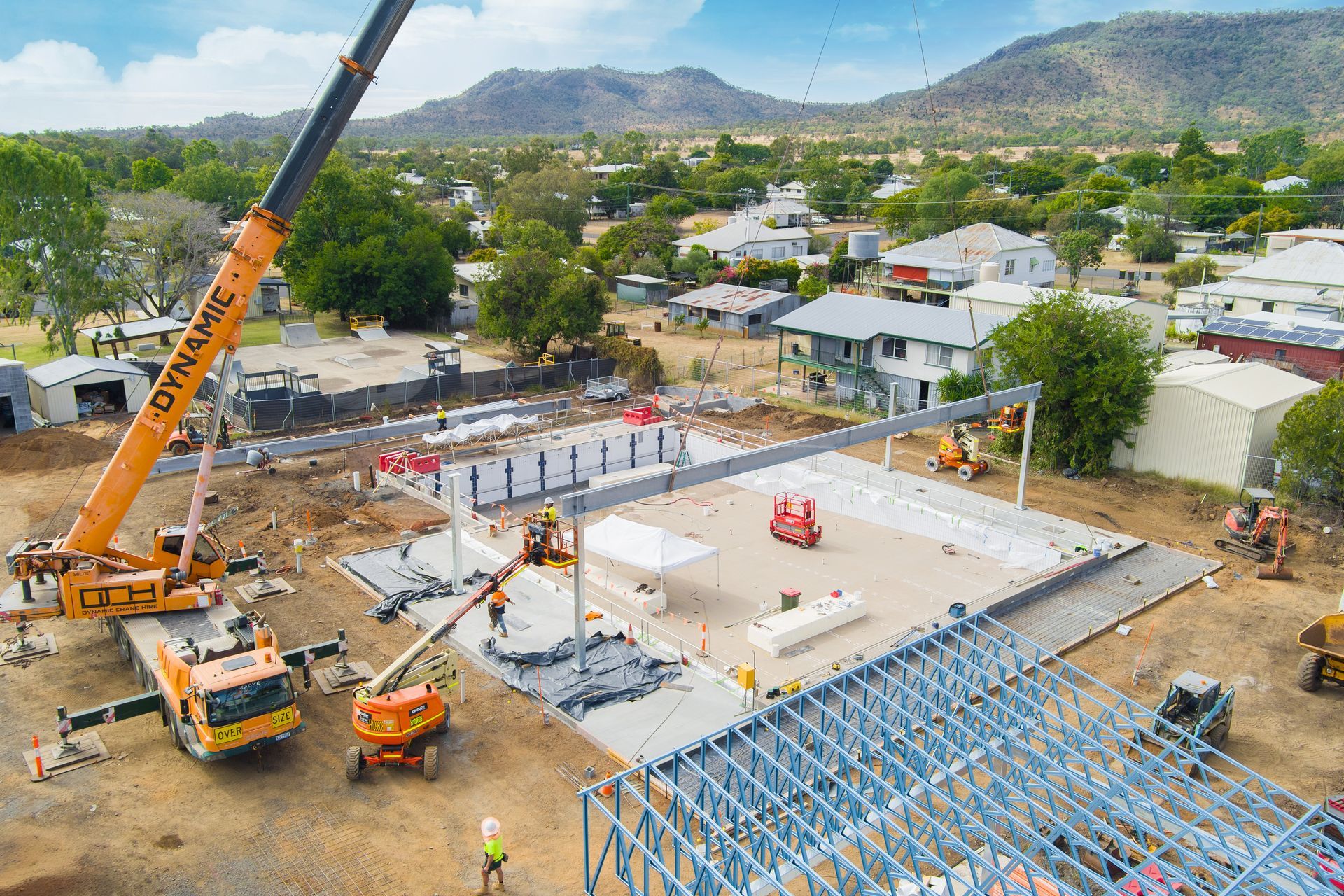 Construction site with crane lifting steel beams; workers on ground — Dynamic Crane Hire In Emerald, QLD