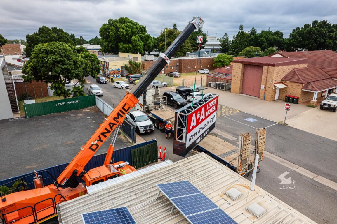 A Crane Is Lifting A Sign On Top Of A Building — Dynamic Crane Hire In Biloela, QLD