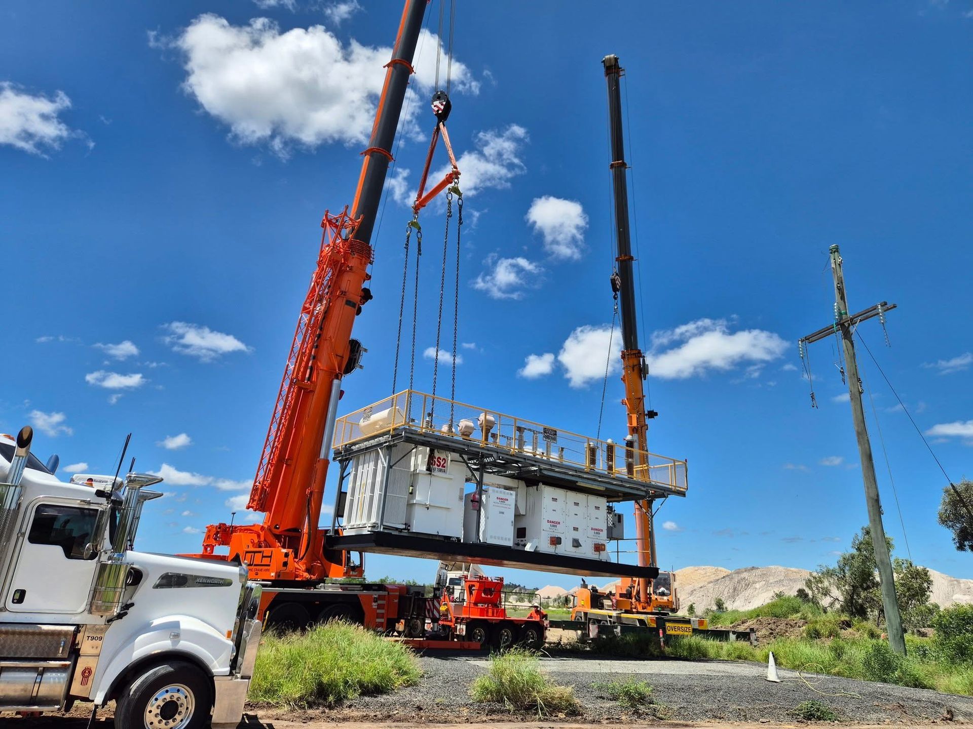 Two cranes lifting a large electrical transformer against a blue sky  — Dynamic Crane Hire In Emerald, QLD