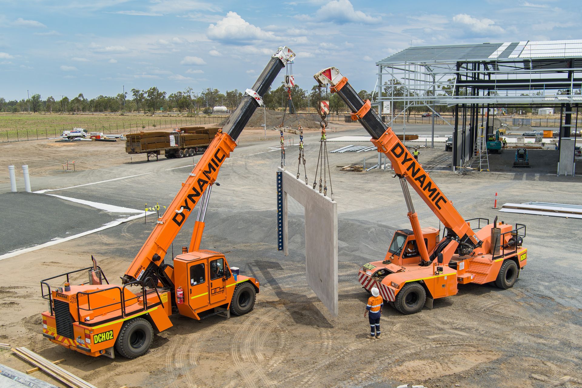 Two Orange Crane Trucks Are Working On A Construction Site — Dynamic Crane Hire In Emerald, QLD