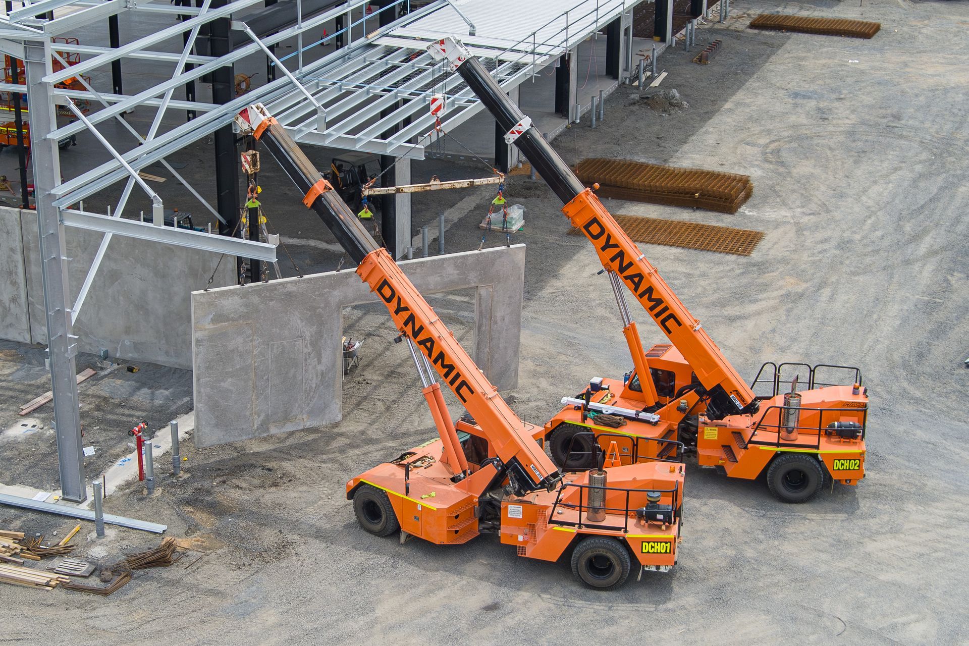 Two Orange Trucks Parked In Front Of A Building Under Construction — Dynamic Crane Hire In Emerald, QLD