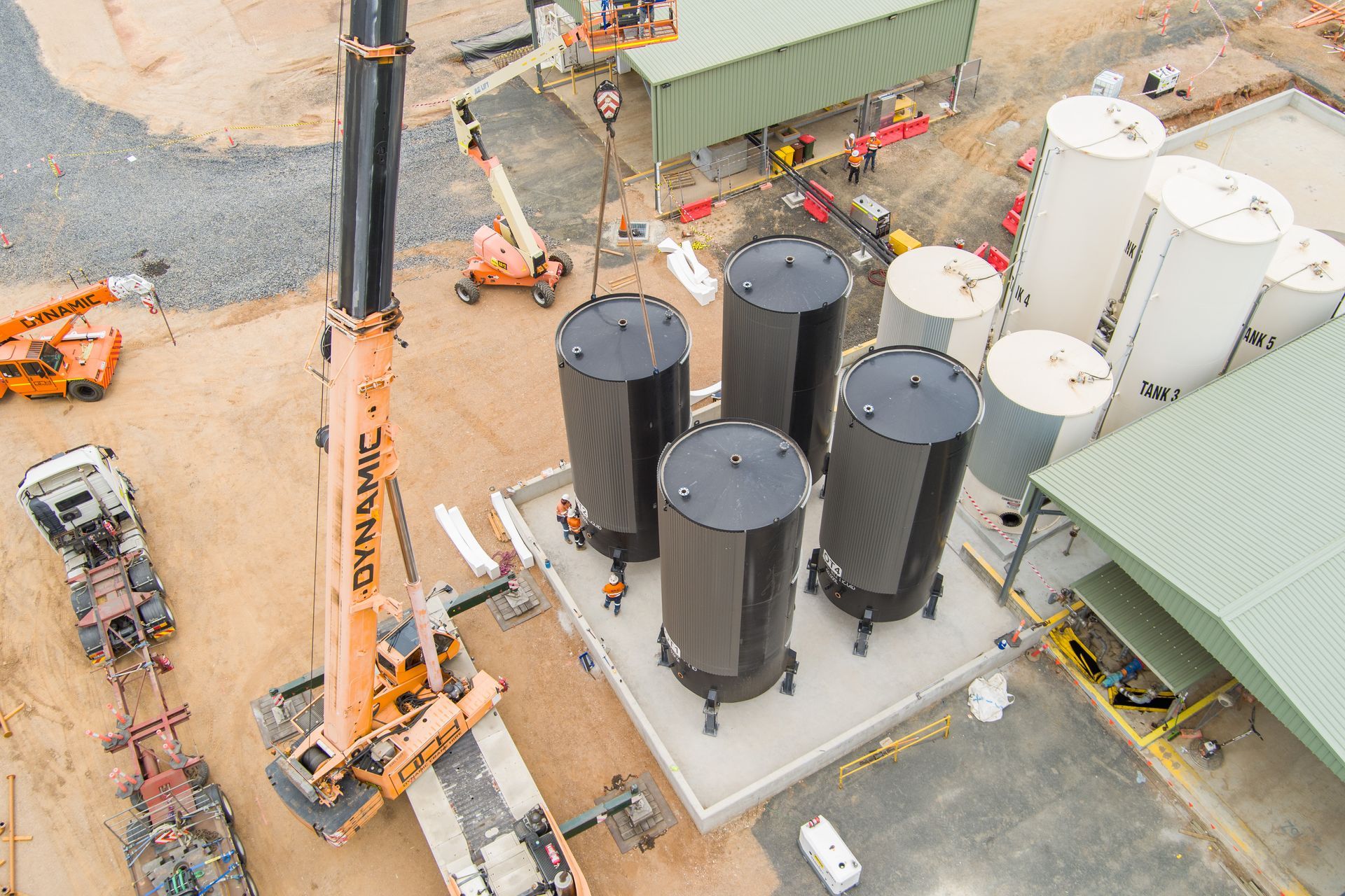Overhead view of a construction site with crane lifting industrial storage tanks; several tanks are already in place — Dynamic Crane Hire In Emerald, QLD