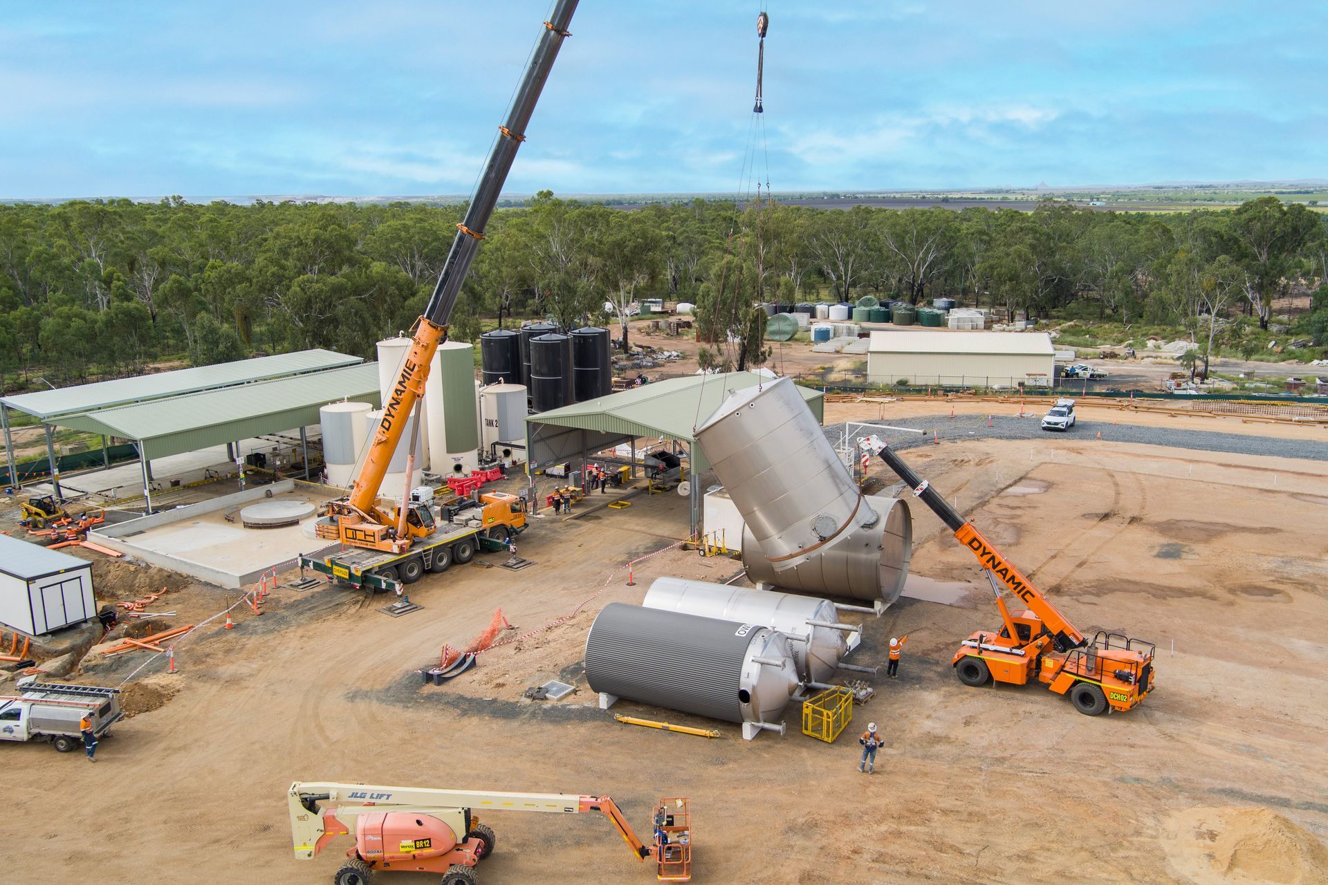 Cranes lifting and positioning large cylindrical tanks at a construction site in a rural setting — Dynamic Crane Hire In Emerald, QLD