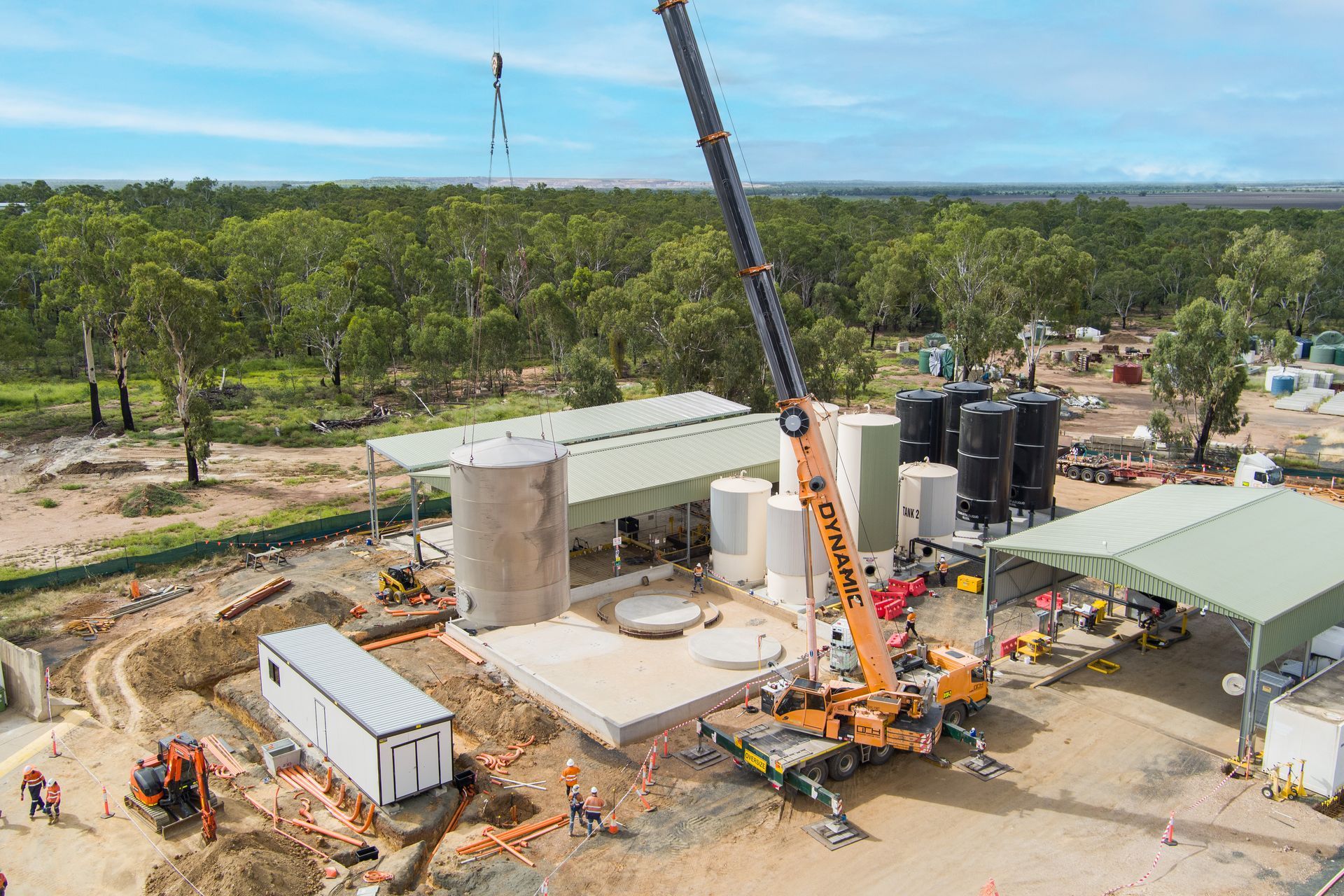 Crane lifting a large cylindrical tank at a construction site surrounded by trees — Dynamic Crane Hire In Emerald, QLD