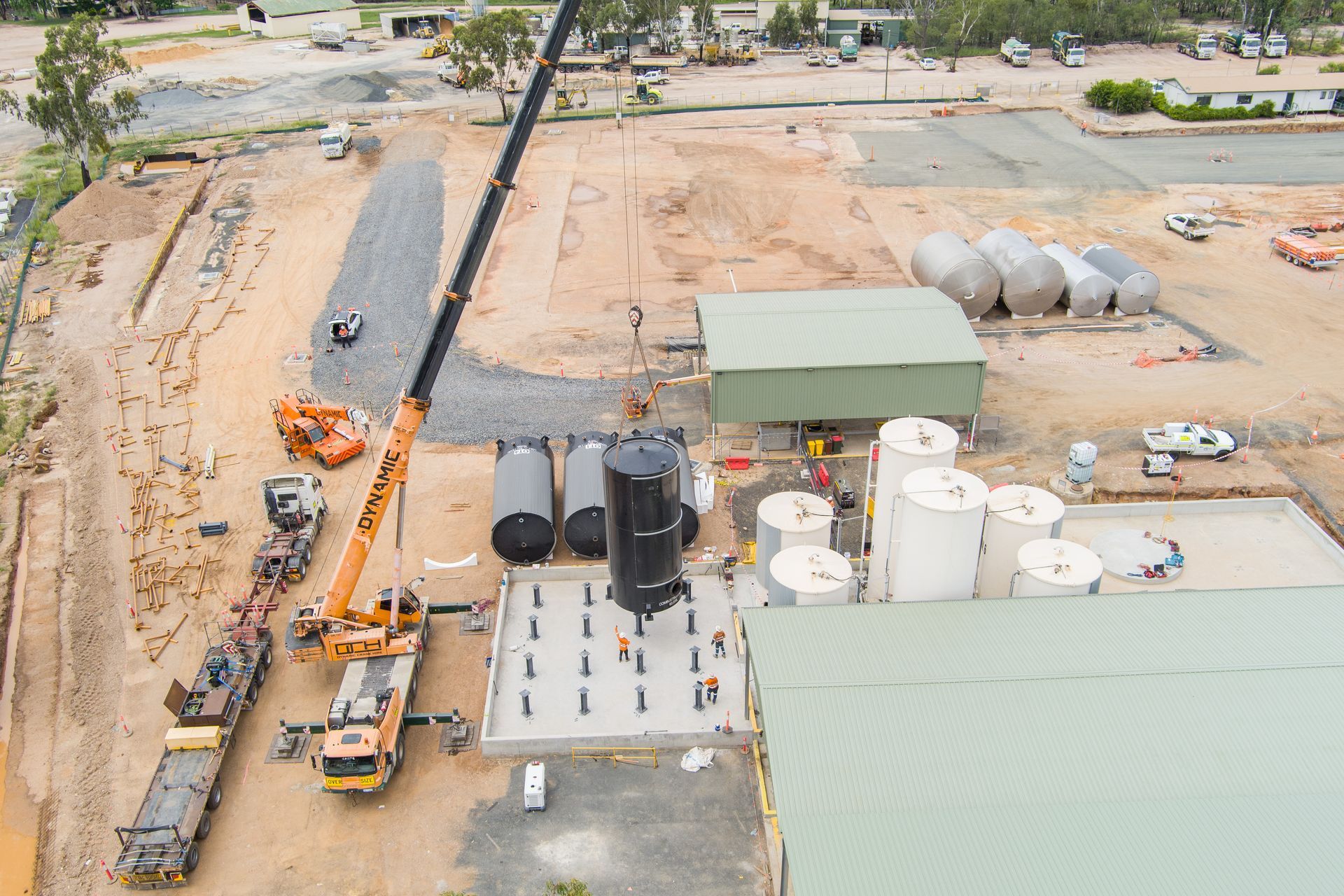 Construction site with crane lifting a large tank, other tanks and buildings nearby — Dynamic Crane Hire In Emerald, QLD