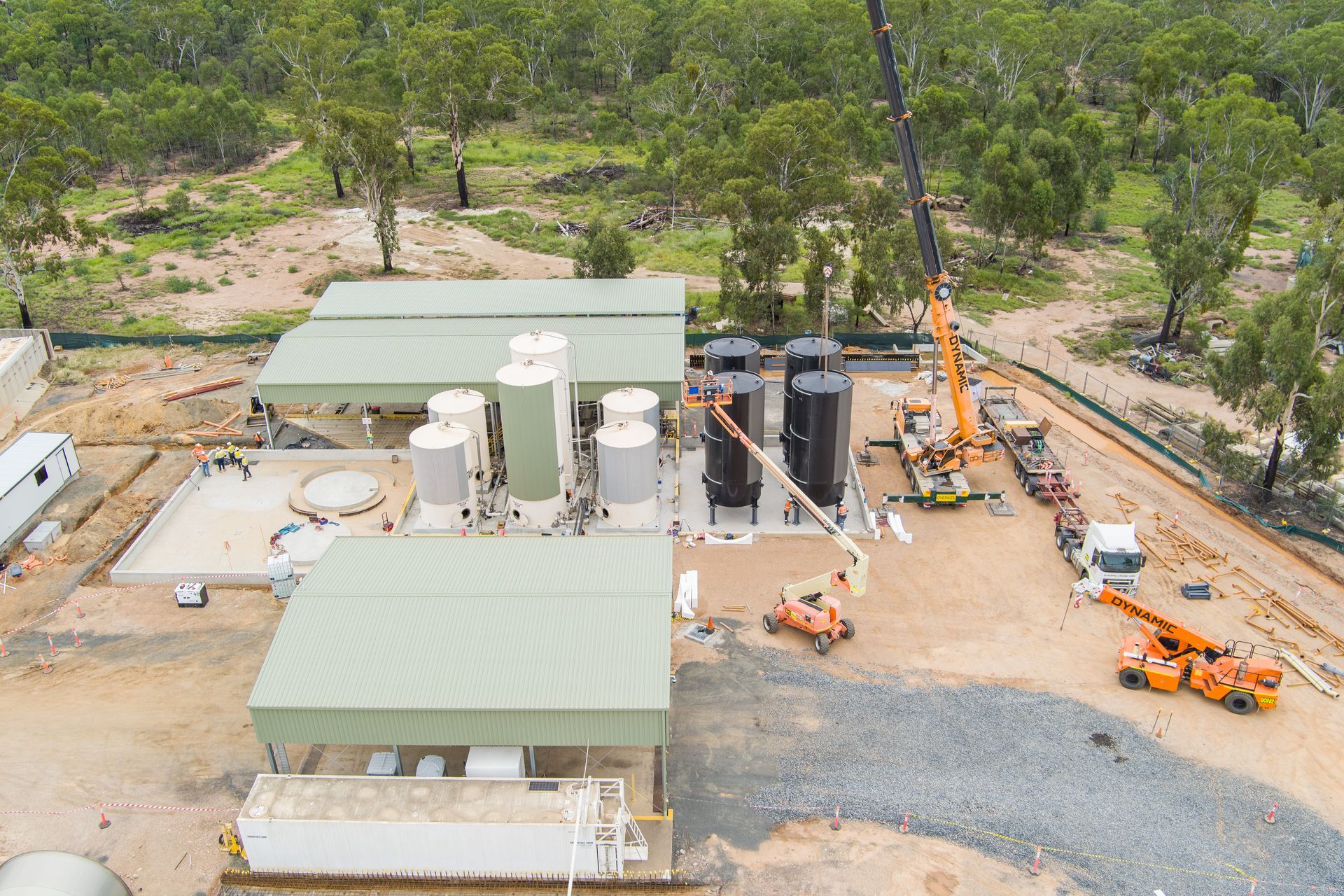 Construction site with storage tanks, sheds, crane, and heavy machinery; set in a wooded area — Dynamic Crane Hire In Emerald, QLD