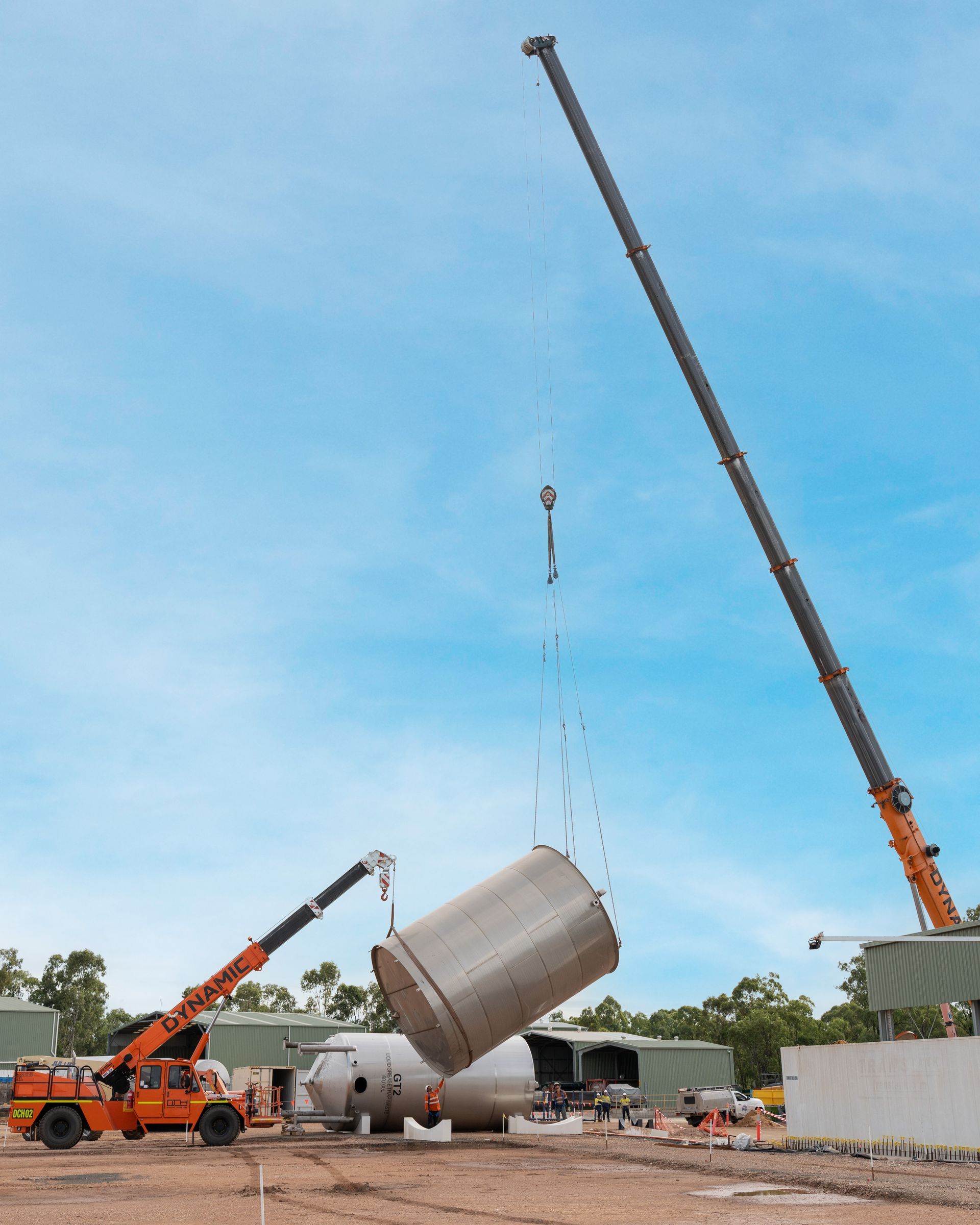 Two cranes lifting a large, cylindrical metal tank at a construction site. Blue sky in the background — Dynamic Crane Hire In Emerald, QLD
