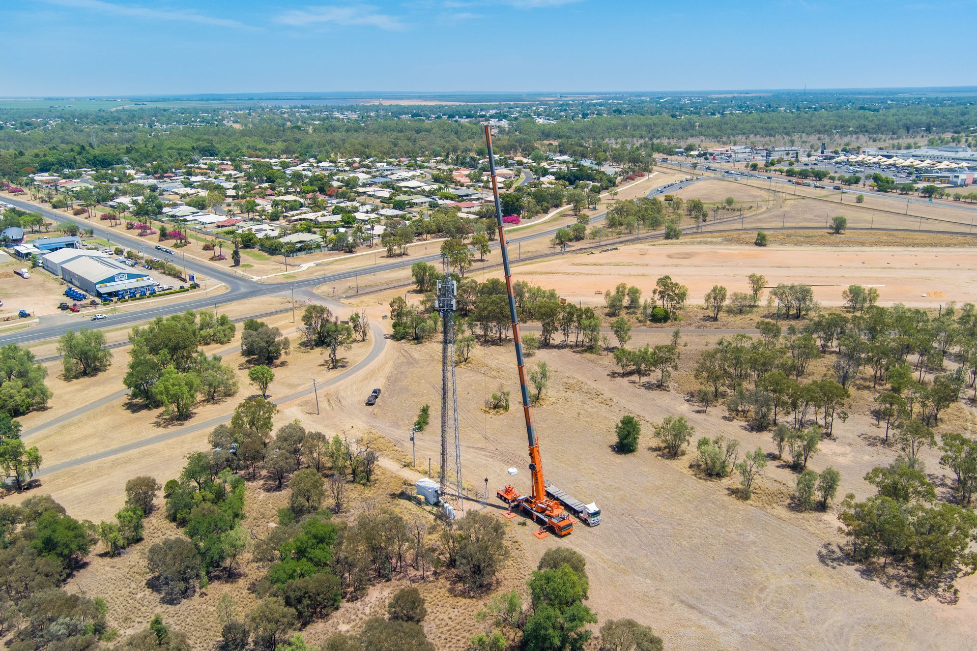 An aerial view of a cell tower under construction in a rural area, with cranes and surrounding buildings — Dynamic Crane Hire In Emerald, QLD