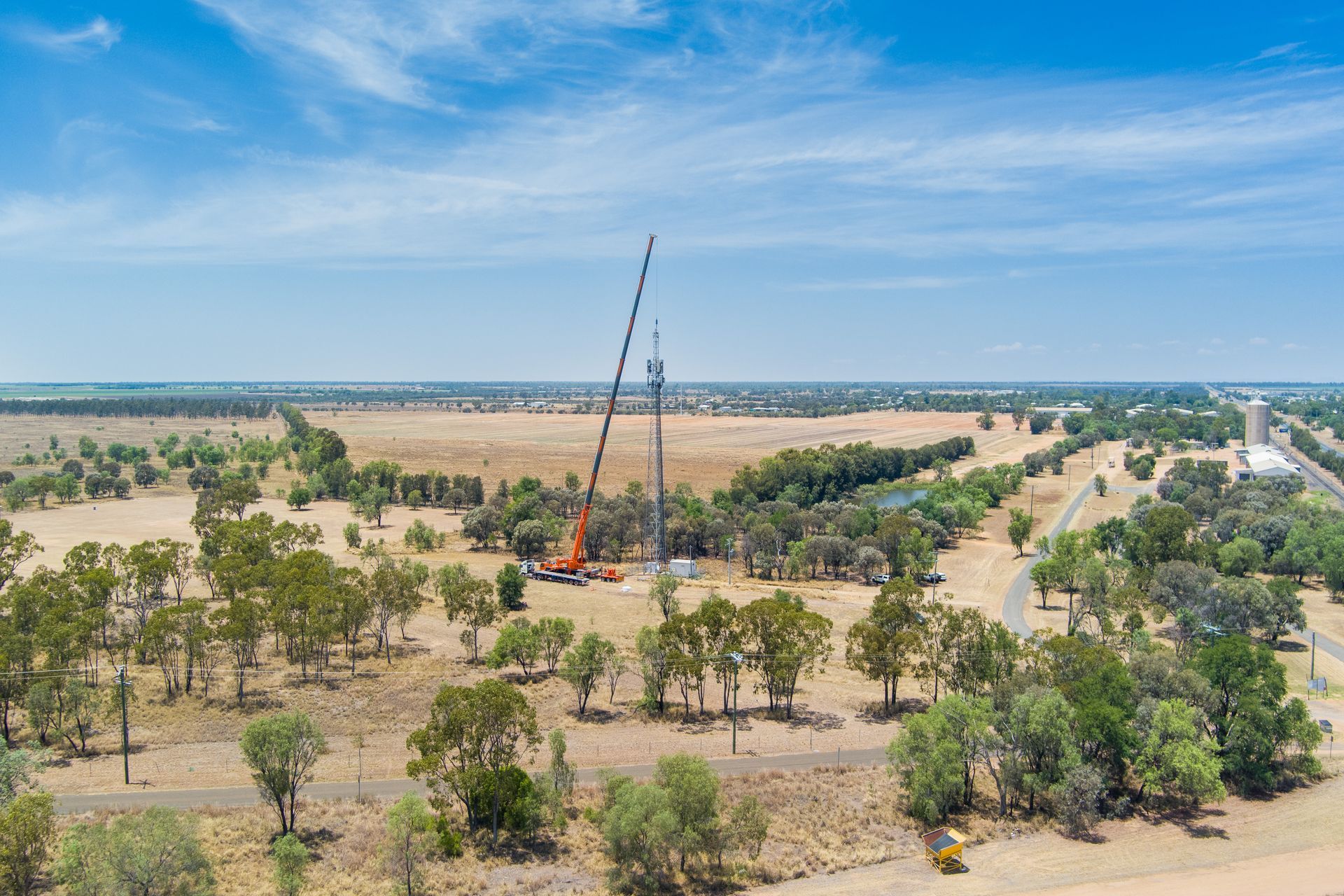 Construction site in a field with a large crane lifting a tower structure. Blue sky, sparse trees — Dynamic Crane Hire In Emerald, QLD