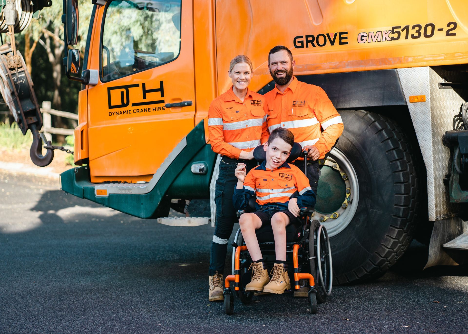 Family in orange work uniforms posing by an orange truck  — Dynamic Crane Hire In Emerald, QLD