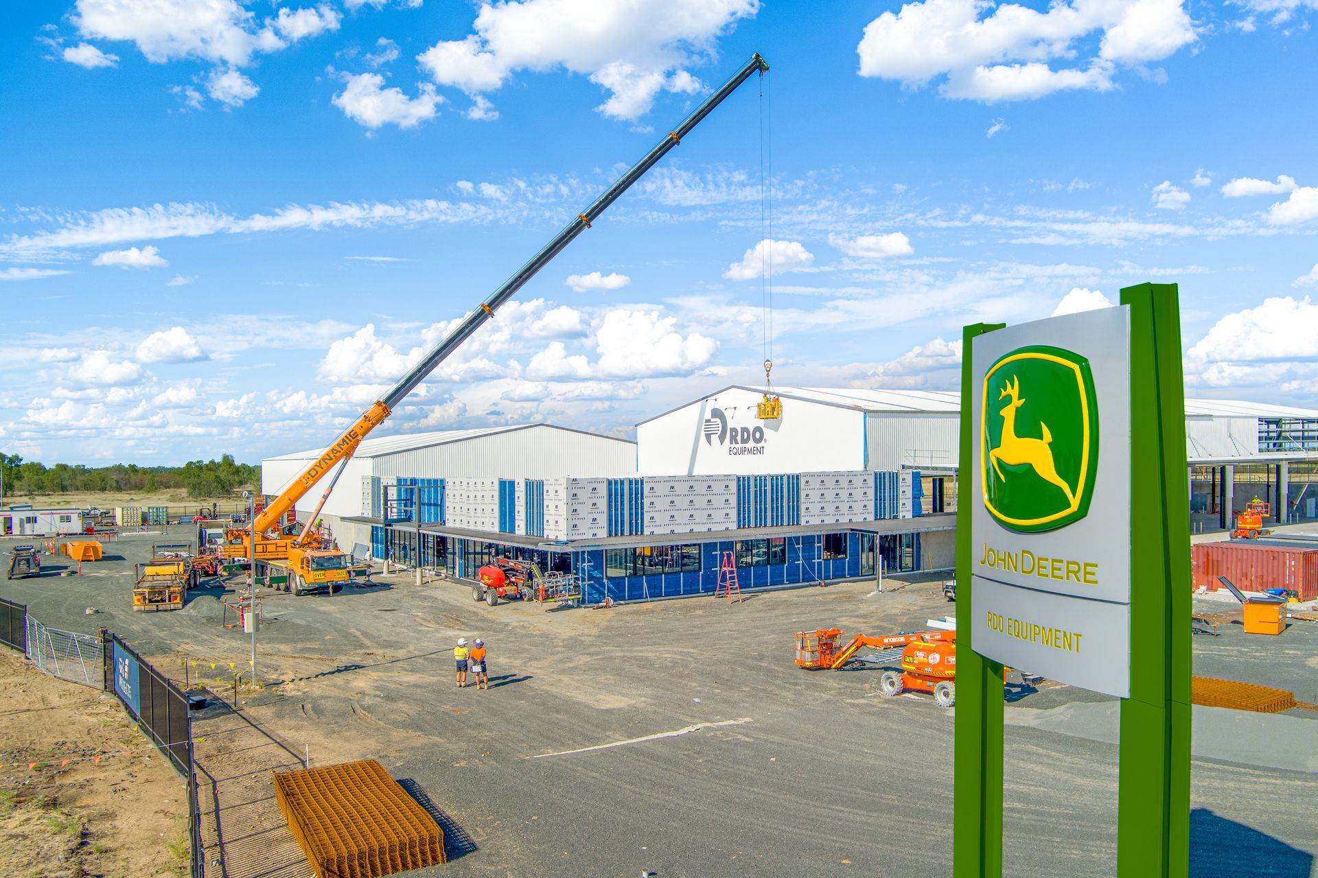 Construction site with John Deere sign; crane lifting container onto building — Dynamic Crane Hire In Emerald, QLD