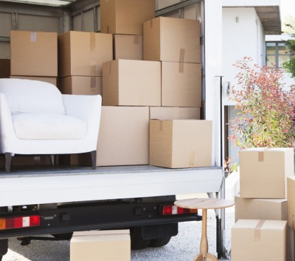 Moving truck loaded with cardboard boxes and a white armchair at a house driveway