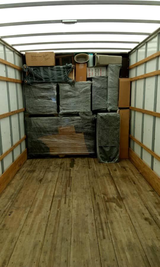 Box truck cargo area loaded with shrink-wrapped furniture and boxes on a wooden floor