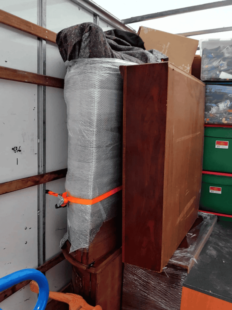 Large wrapped furniture secured with orange straps inside a moving truck or storage trailer.