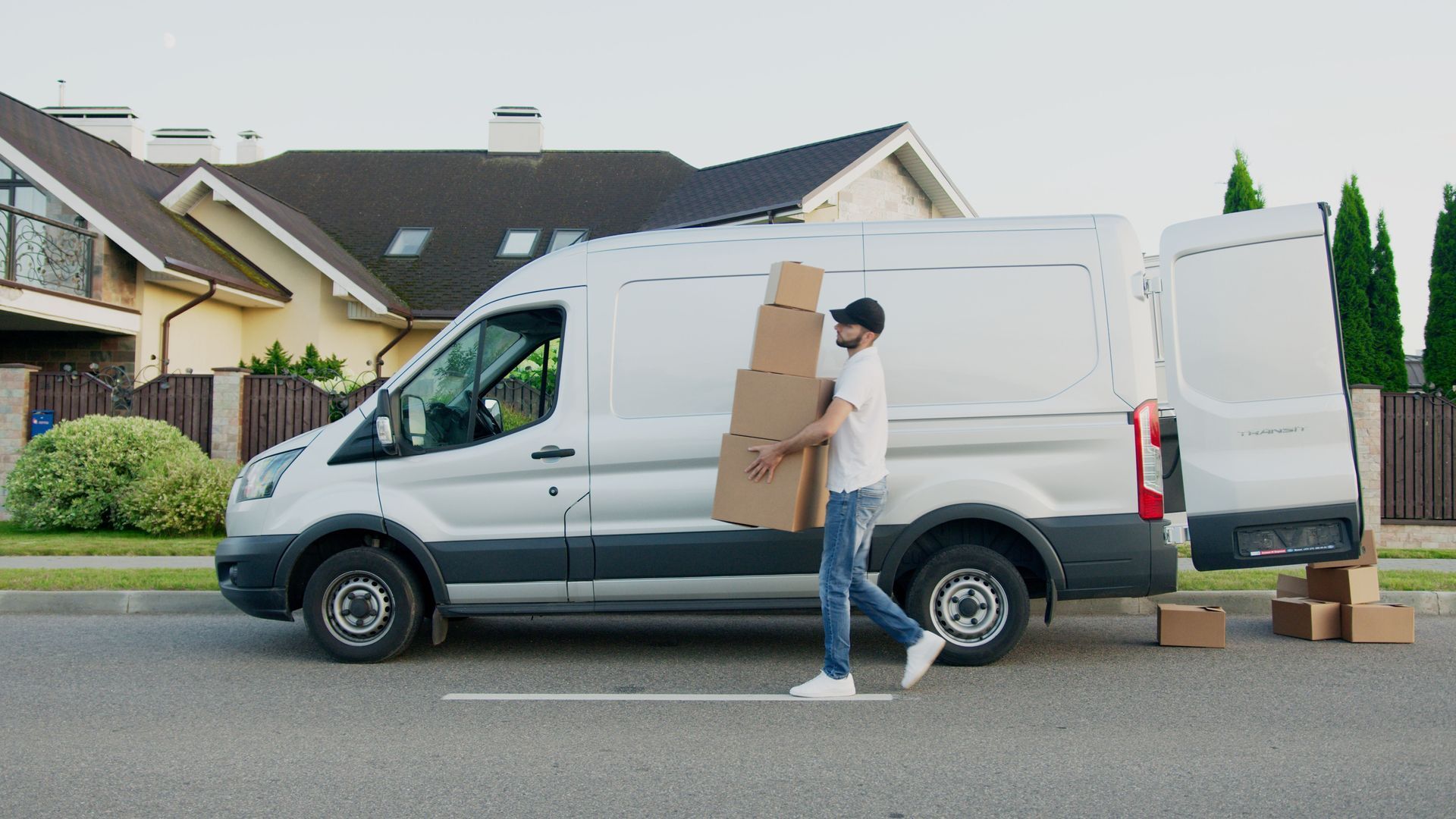 Person carrying boxes beside a white delivery van on a suburban street
