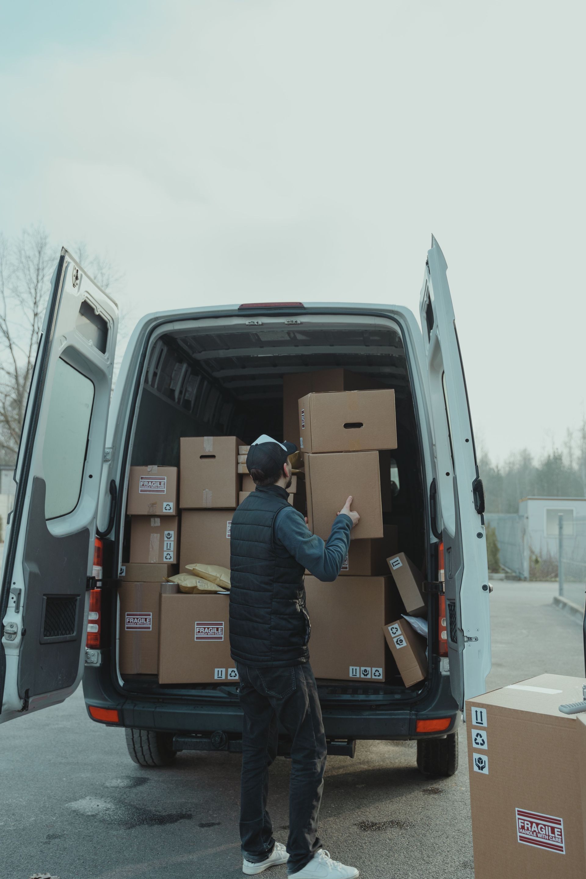 Person loading boxes into the back of a white delivery van outdoors on a cloudy day