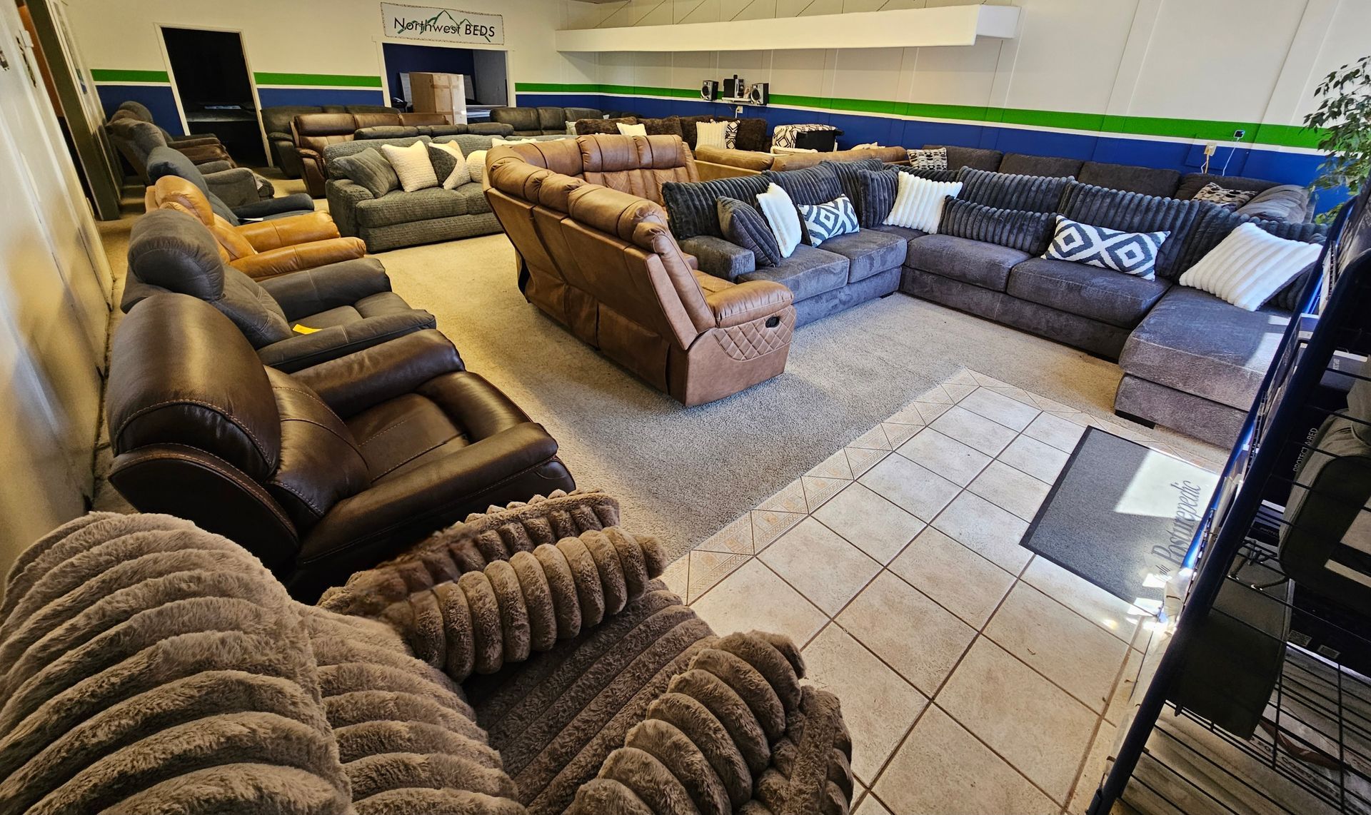 Living room — Springfield, OR — Northwest Home Furnishings A showroom featuring various recliners and sectionals in brown, gray, and tan, arranged on carpet and tiled flooring.