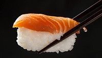 Sushi nigiri held by chopsticks against a dark background, delicious salmon