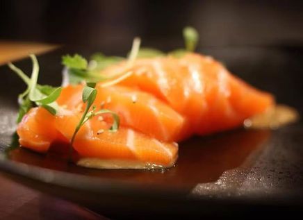 Fresh salmon sashimi, garnished with sprouts, served on black plate