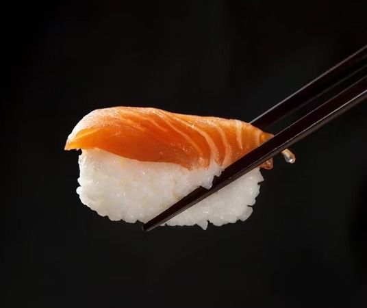 Salmon nigiri sushi held with chopsticks on a black background