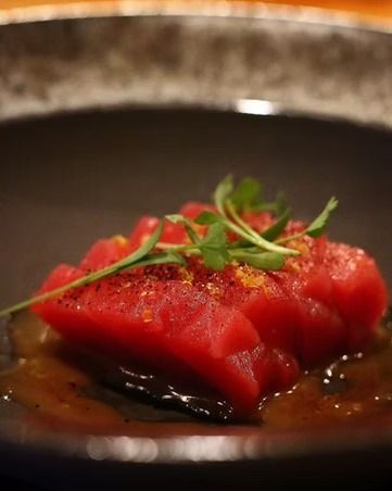 Red tuna sashimi garnished with herbs in a dark bowl, close-up.
