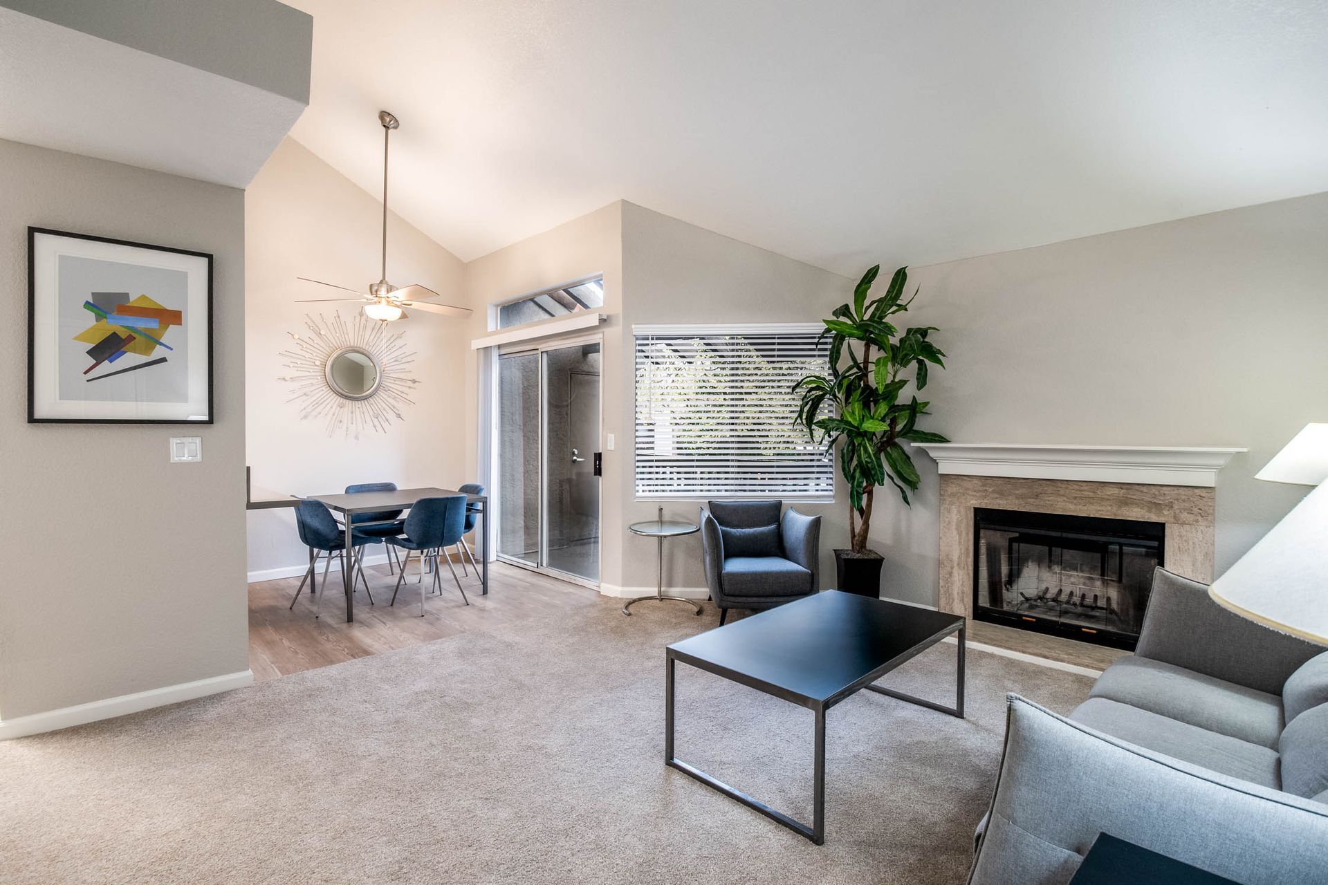 Living room in an apartment with a gray sofa, fireplace, plant, and dining area at Shore Park at Riverlake.