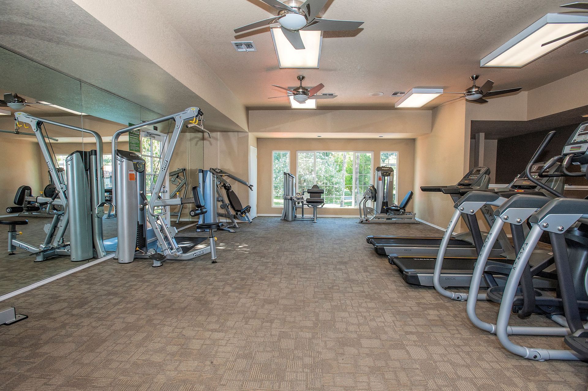 Bright community gym with treadmills, weight machines, and a large window at Shore Park at Riverlake.