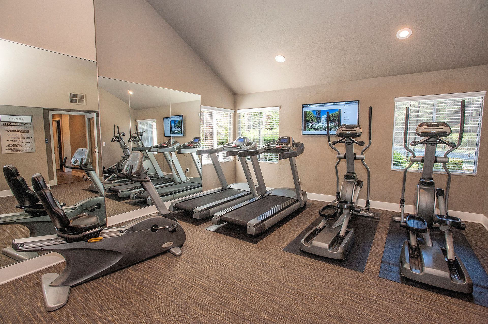Indoor fitness center with treadmills, ellipticals, a stationary bike, and a mirrored wall at Shore Park at Riverlake.
