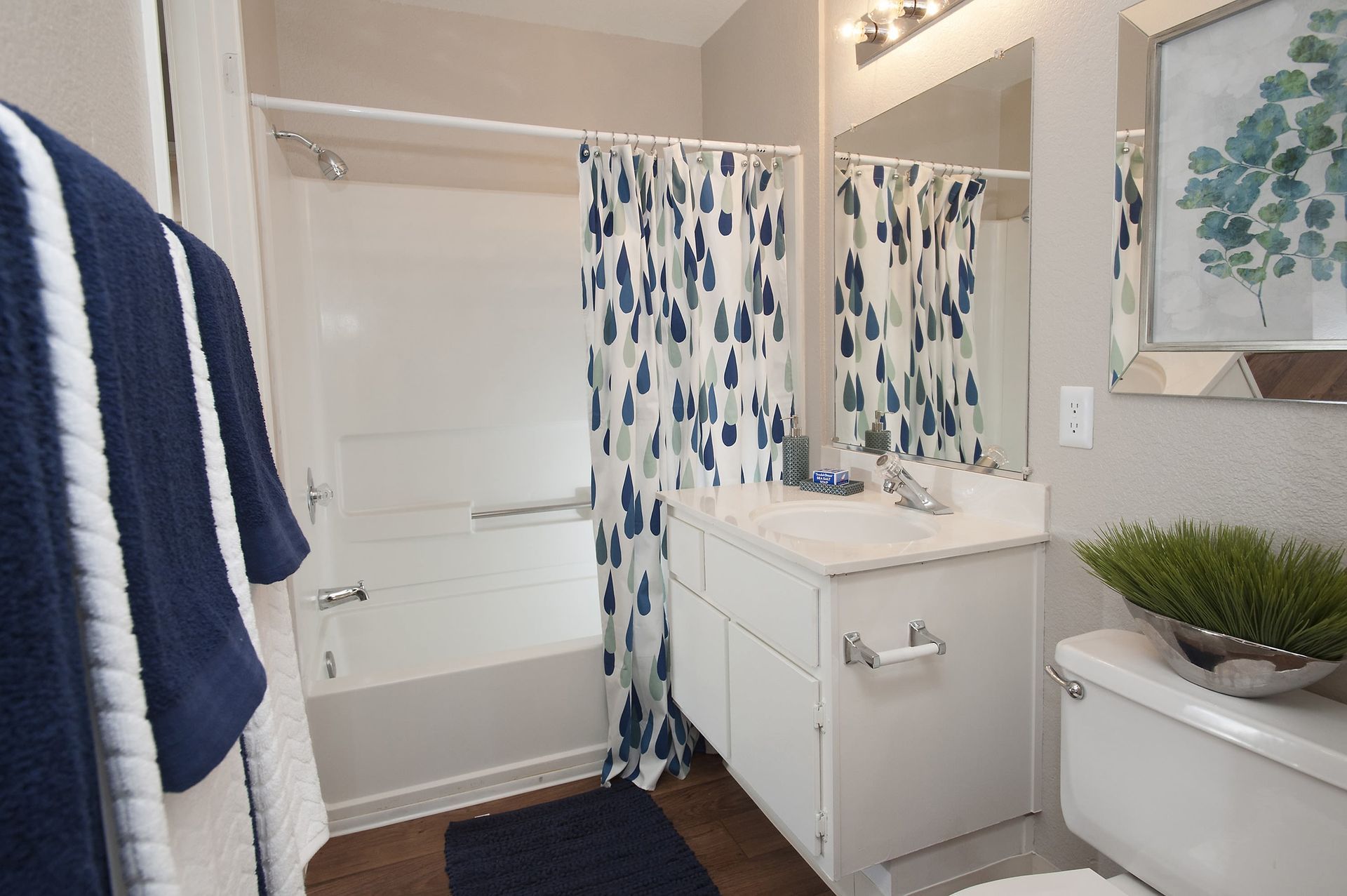 Bright bathroom with white vanity, mirror, tub/shower, and a blue teardrop-pattern shower curtain at Shore Park at Riverlake.