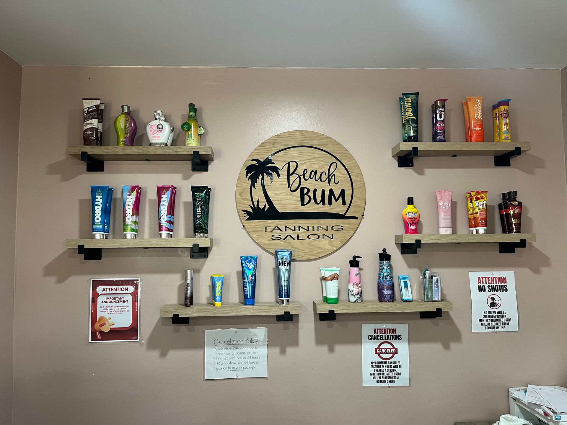 Three industrial pipe shelves mounted on a wall, holding rows of colorful, matching bottles, with plastic bins below.