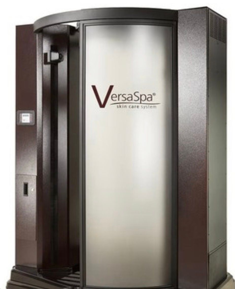 A red, cylindrical stand-up tanning bed centered in a small, wood-floored room next to a small shelving unit.