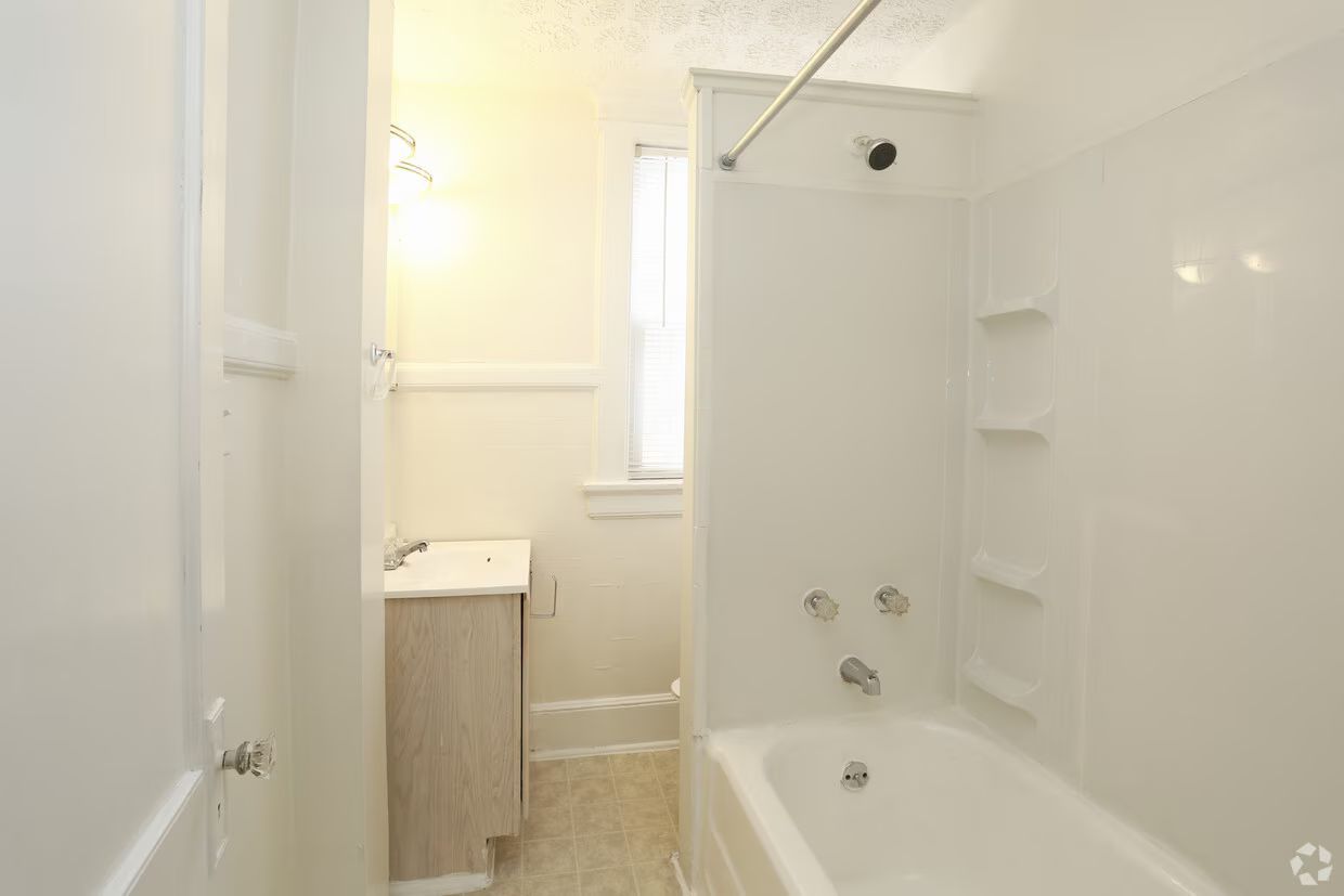 Bright white bathroom with a bathtub, shower, window, and small vanity sink