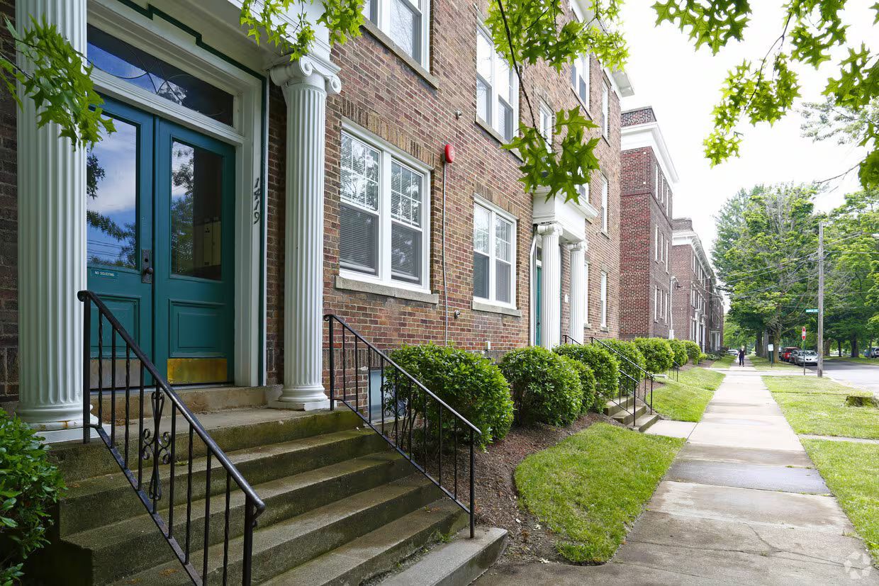 Brick apartment building entrance with steps, teal door, and tree-lined sidewalk
