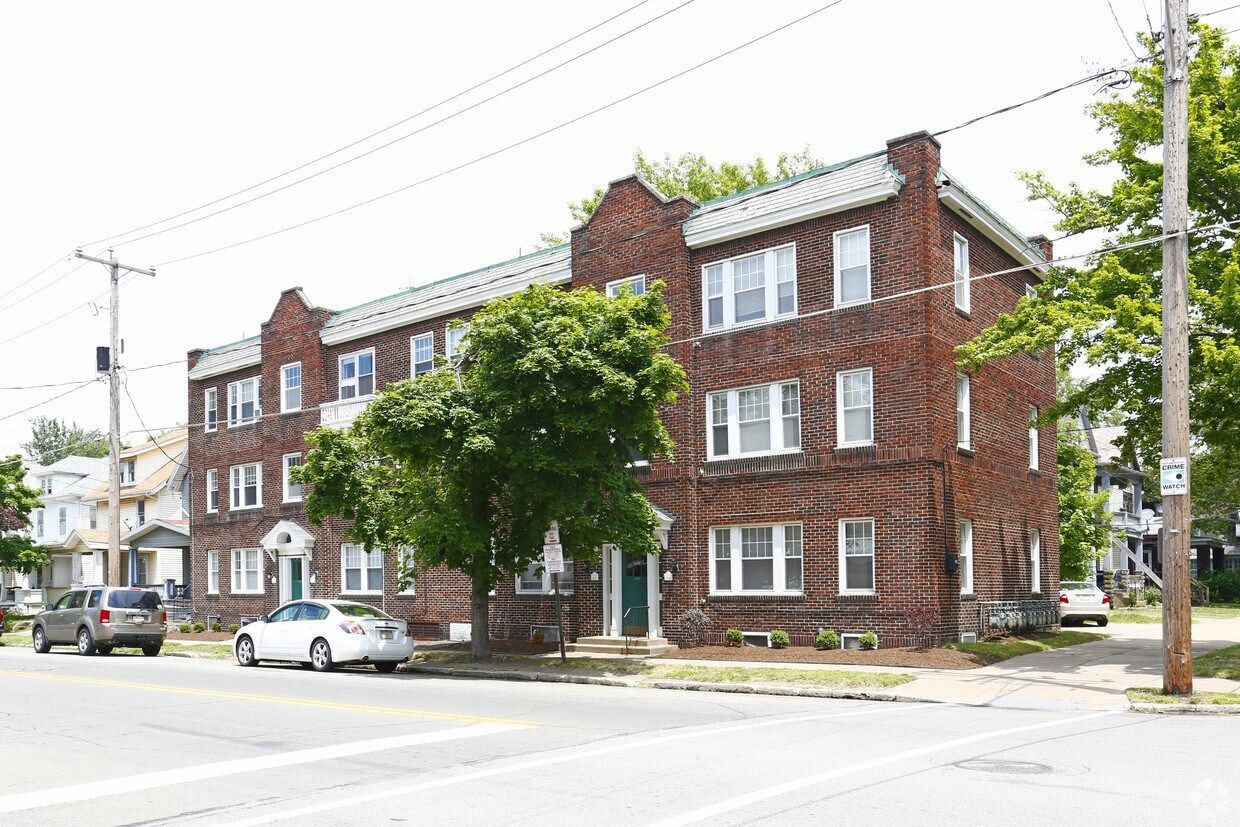 Brick apartment building on a street corner with parked cars and a tree in front