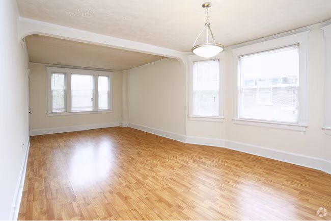 Empty beige living room with hardwood floors and large windows letting in bright daylight