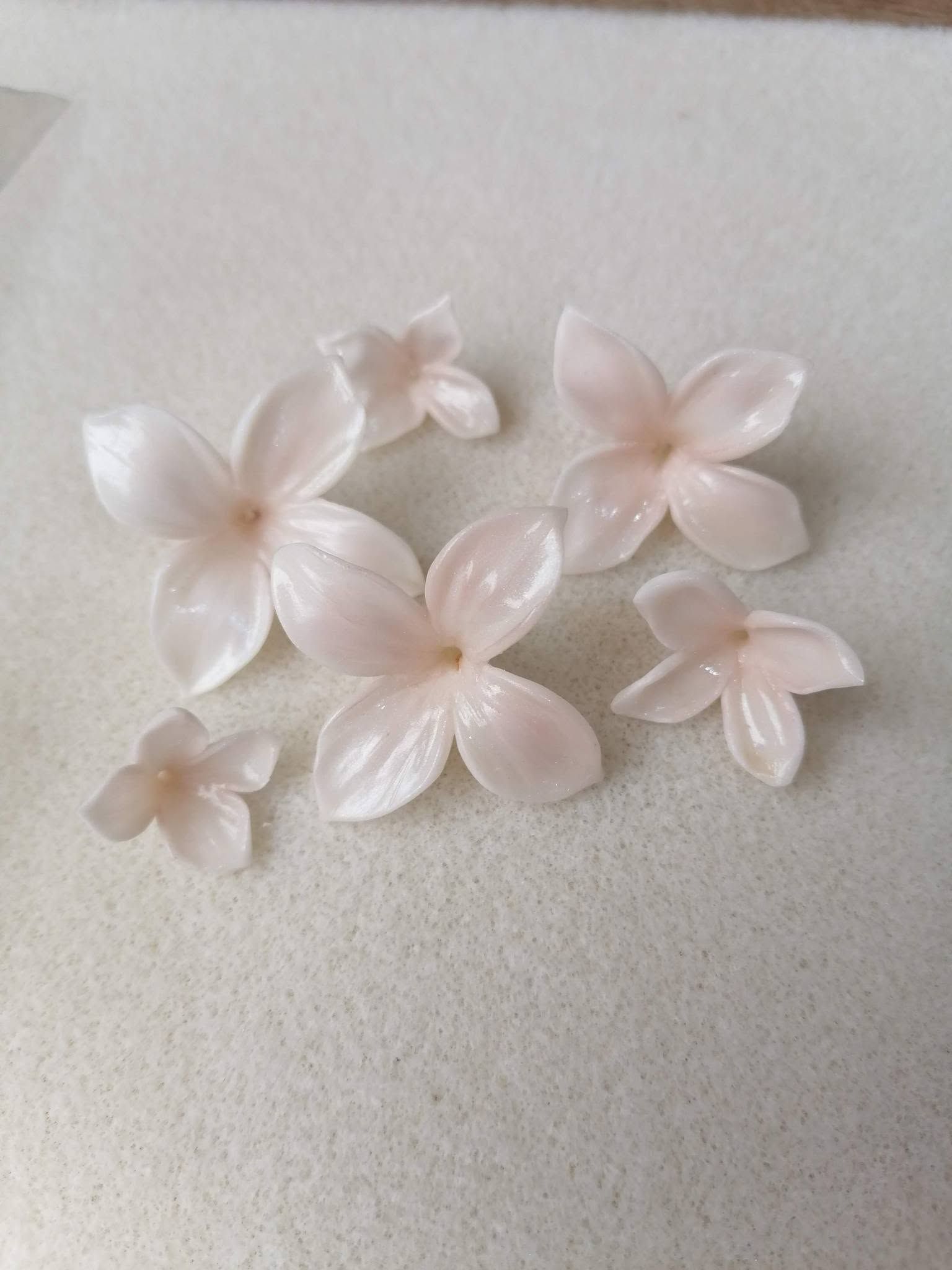 Pequeñas cuentas translúcidas de color rosa pálido con forma de flor, esparcidas sobre una superficie gris claro